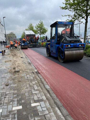 Wals verdicht de rode deklaag van een fietspad, spreidmachine op de achtergrond